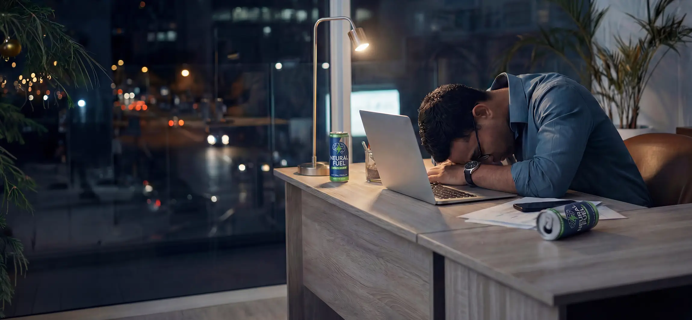A social worker that feel sleep at his desk because he worked at= 12 hour day. The sun has gone down and he has a few energy drinks at his desk.
