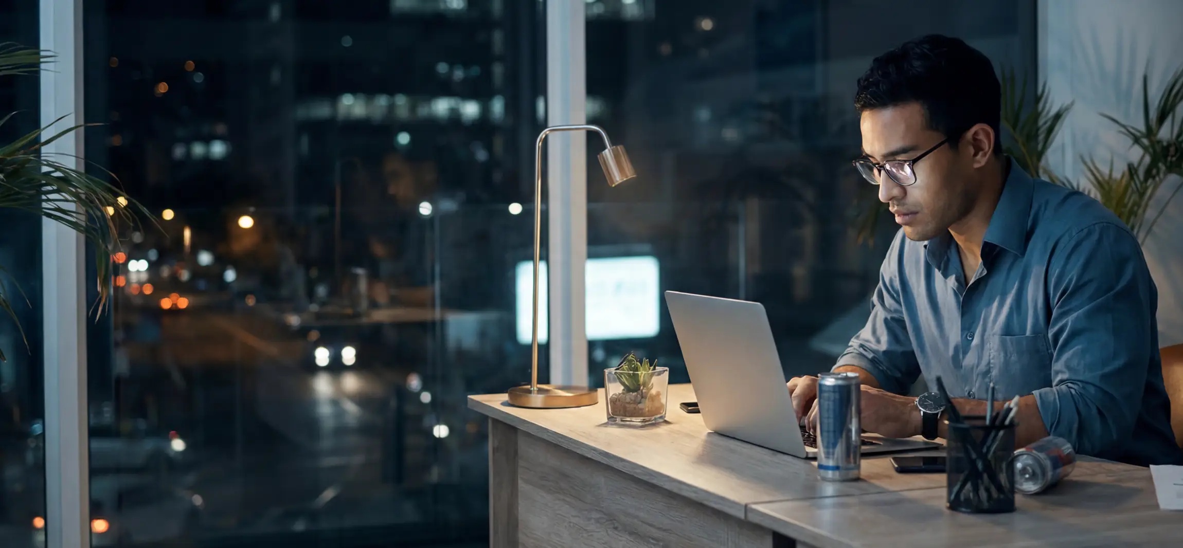 A social worker working at his desk working at night. The sun has gone down and he has a few energy drinks at his desk.