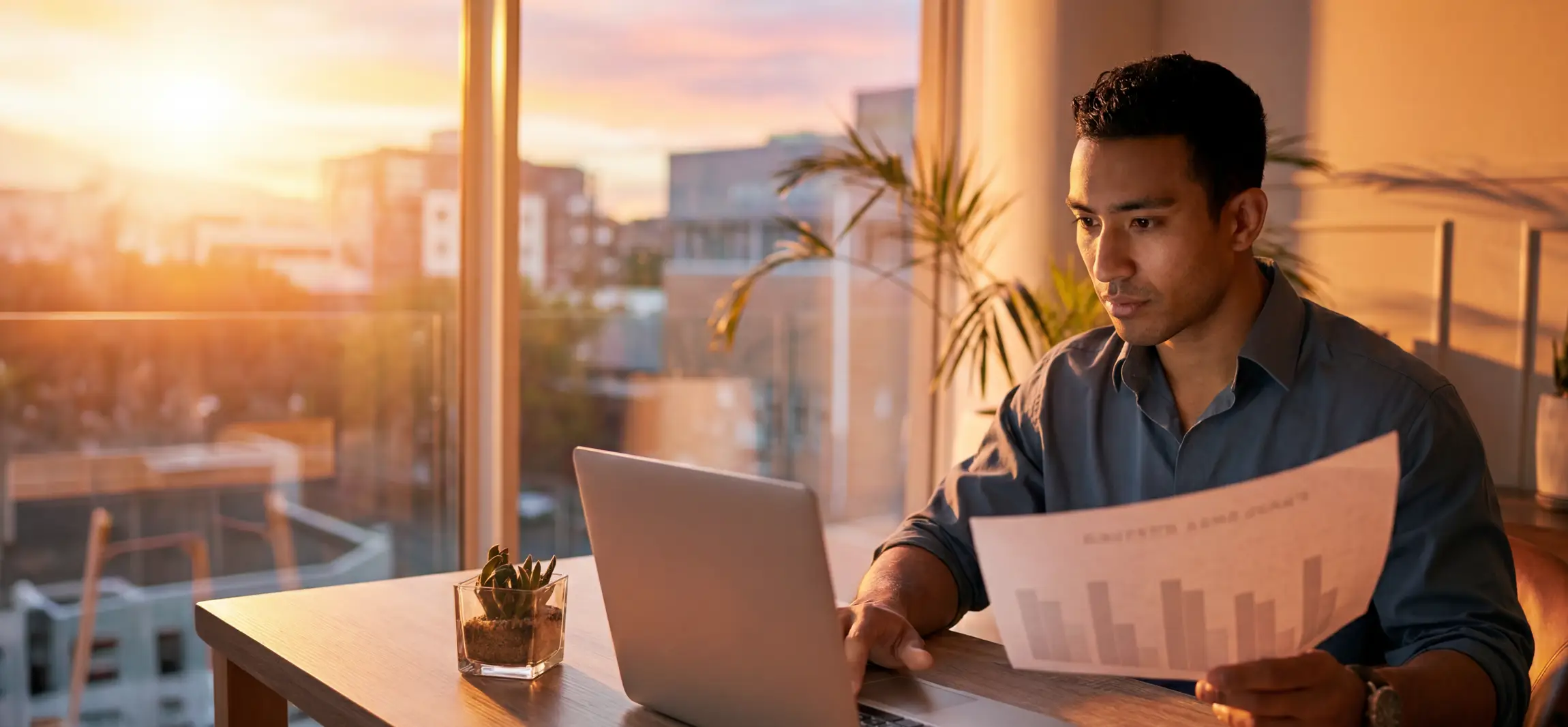 A social worker working at his desk wroking late on his laptop. The sun is starting to set.